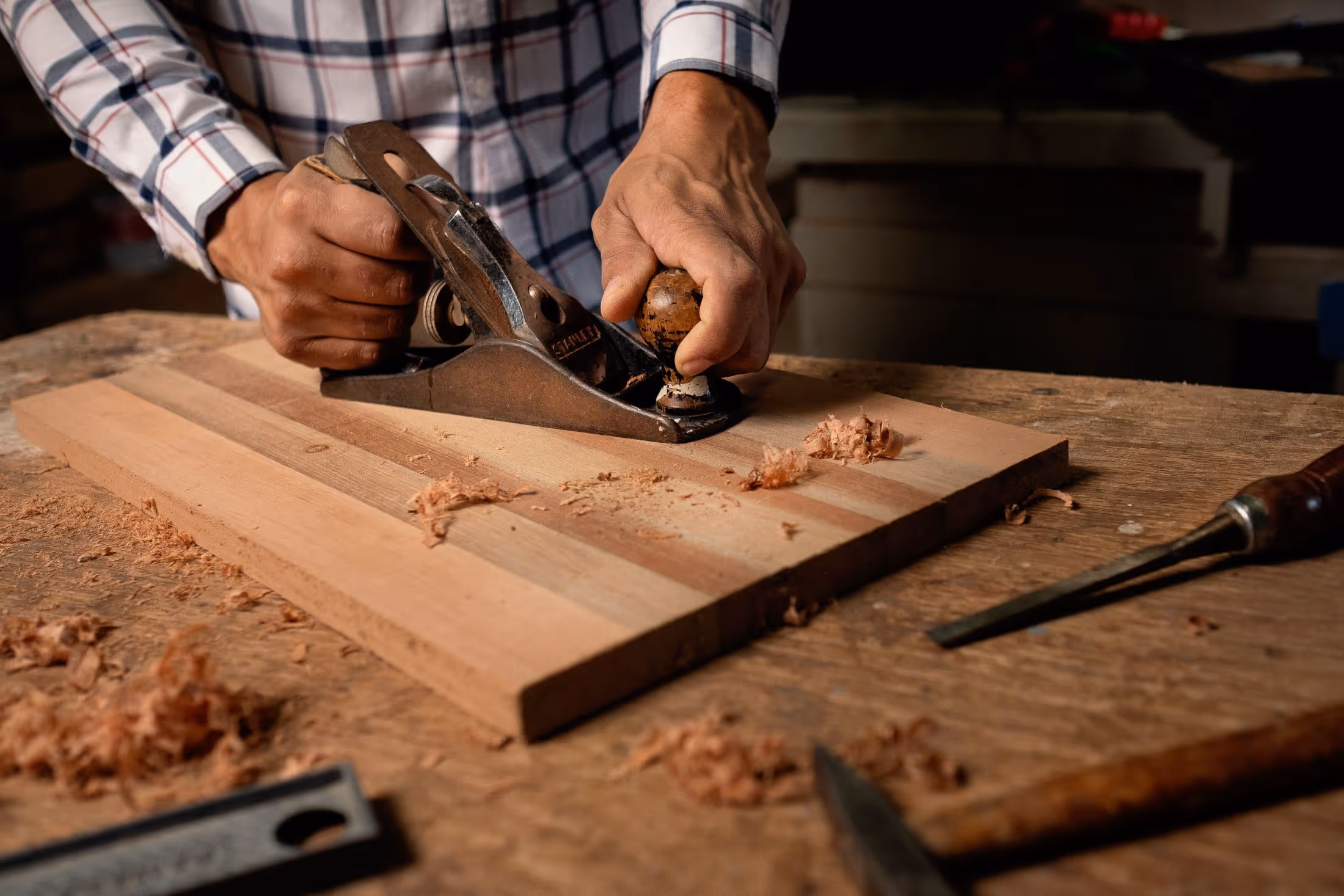 Close-up of a carpenter's hands planing a cedar board with a hand plane